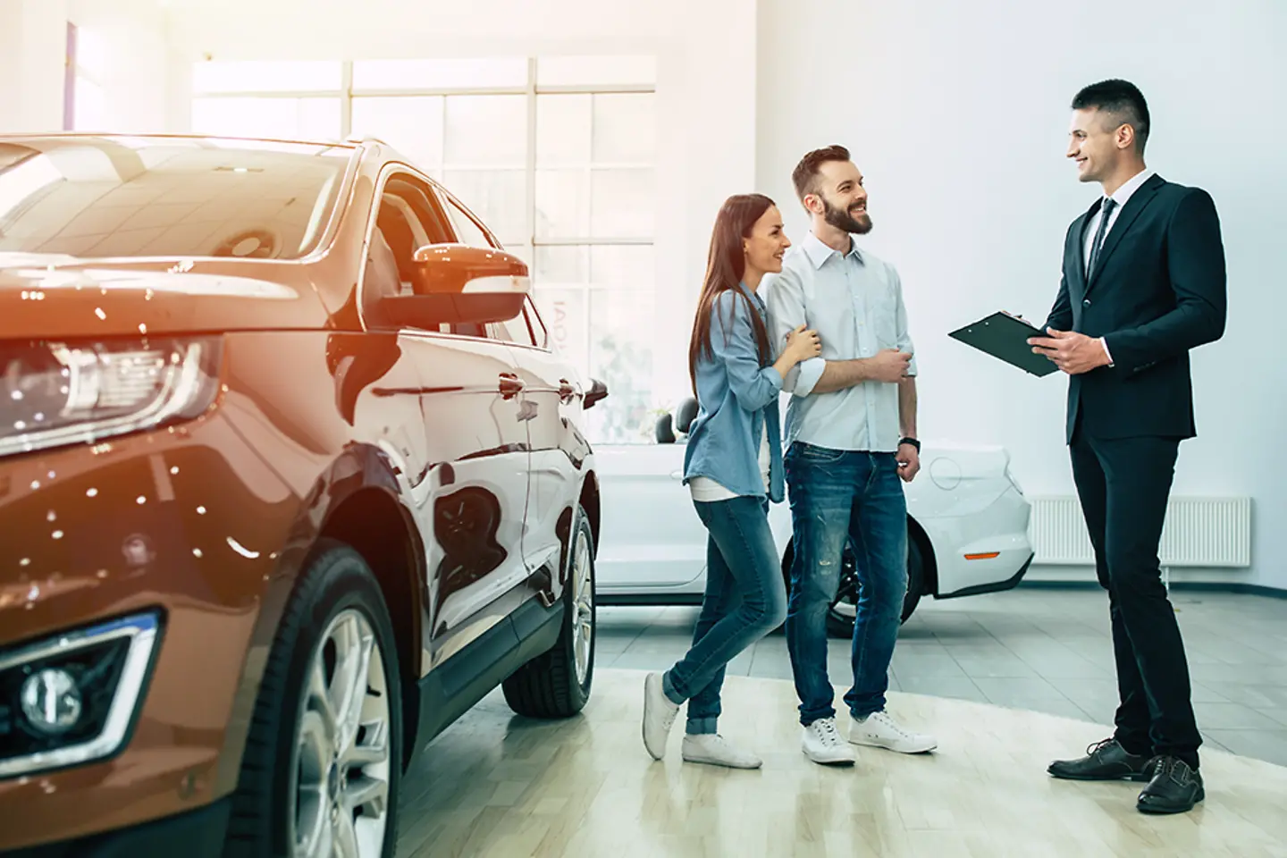 Um jovem casal em uma concessionária de automóveis está conversando com um vendedor.