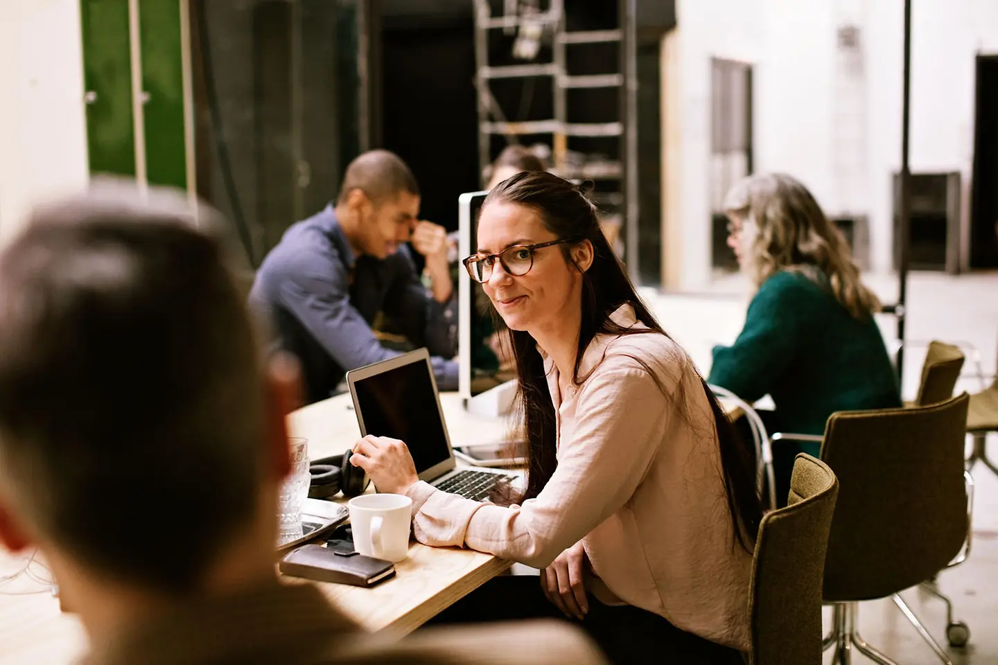 A young mother is sitting at a work desk with colleagues in front of her laptop