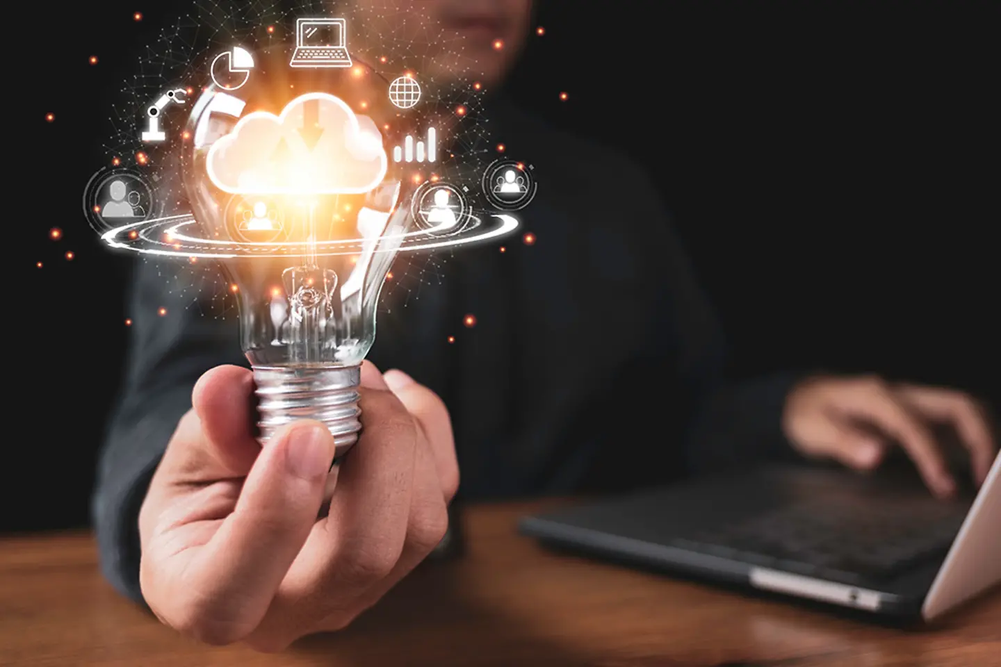 Hand holding lightbulb with cloud computing and technology icons such as laptop computer graph