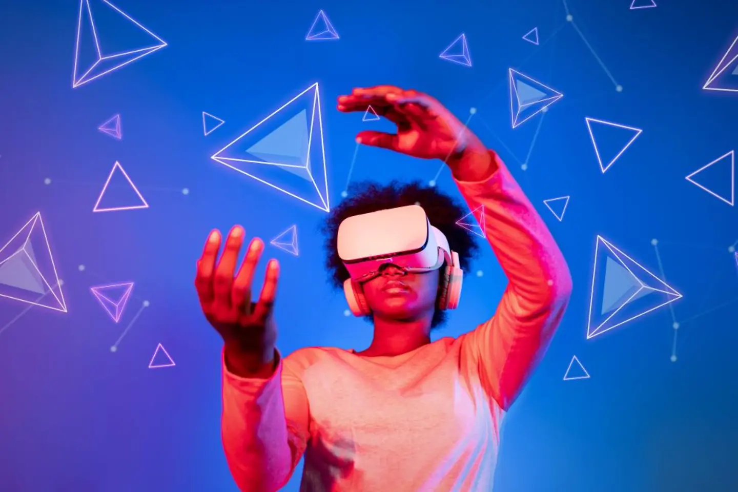 African woman with VR glasses standing at blue and pink background and looking at floating geometric shape