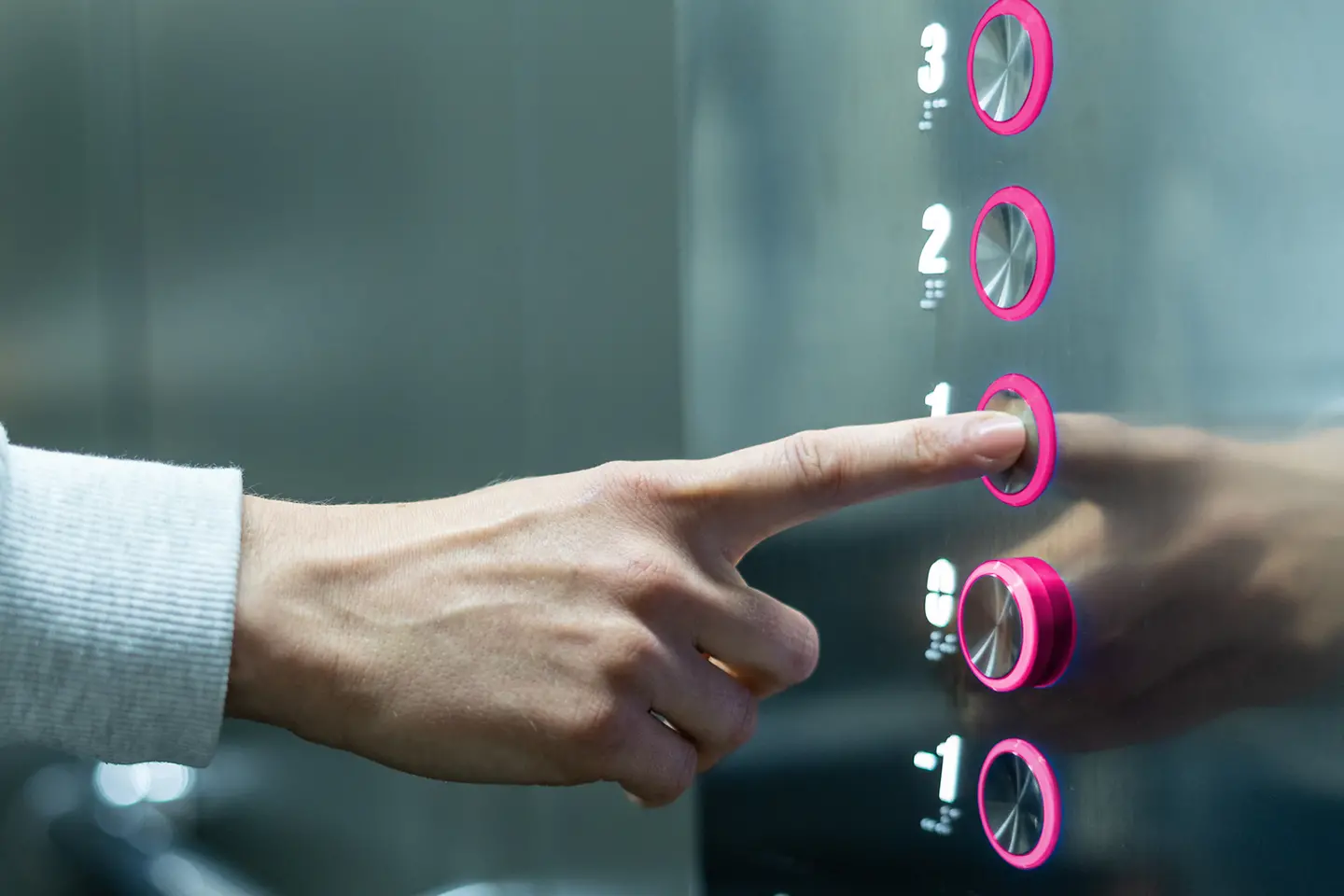 Een magentakleurige knop wordt ingedrukt door een persoon in de lift