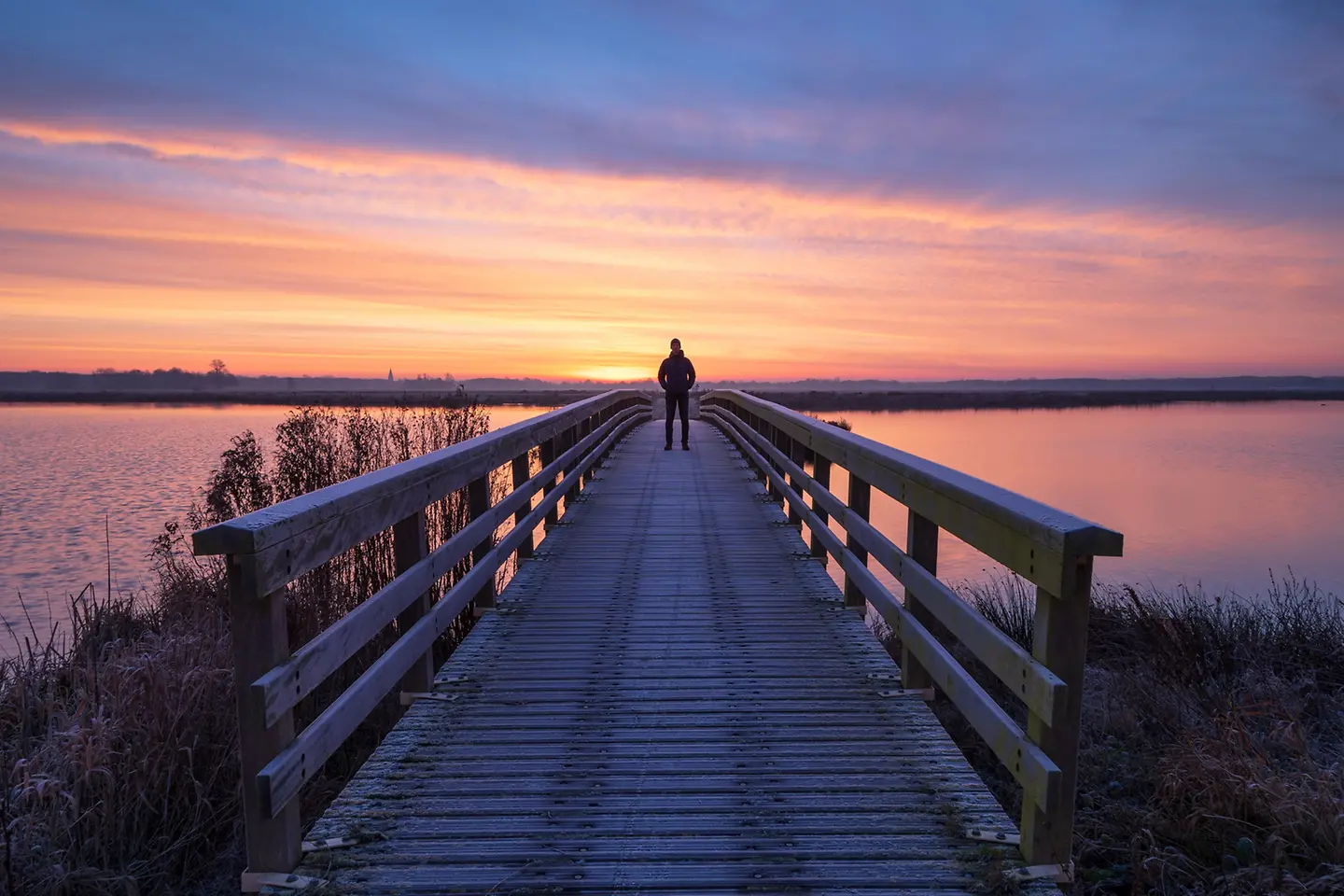 Een man op een houten brug geniet van het uitzicht tijdens een vredige zonsopgang.