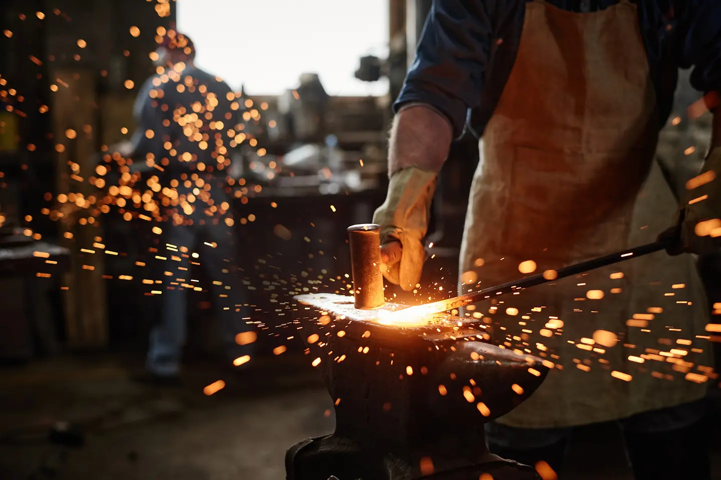 Close-up of blacksmith in apron working with hammer and iron in the workshop