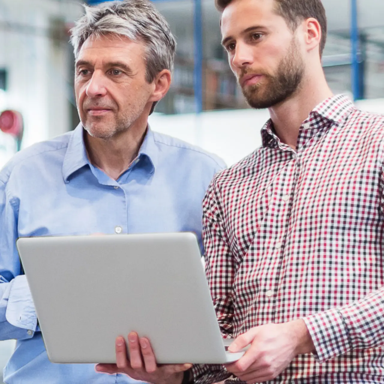 Two businessmen with a laptop in a factory hall focusing on something