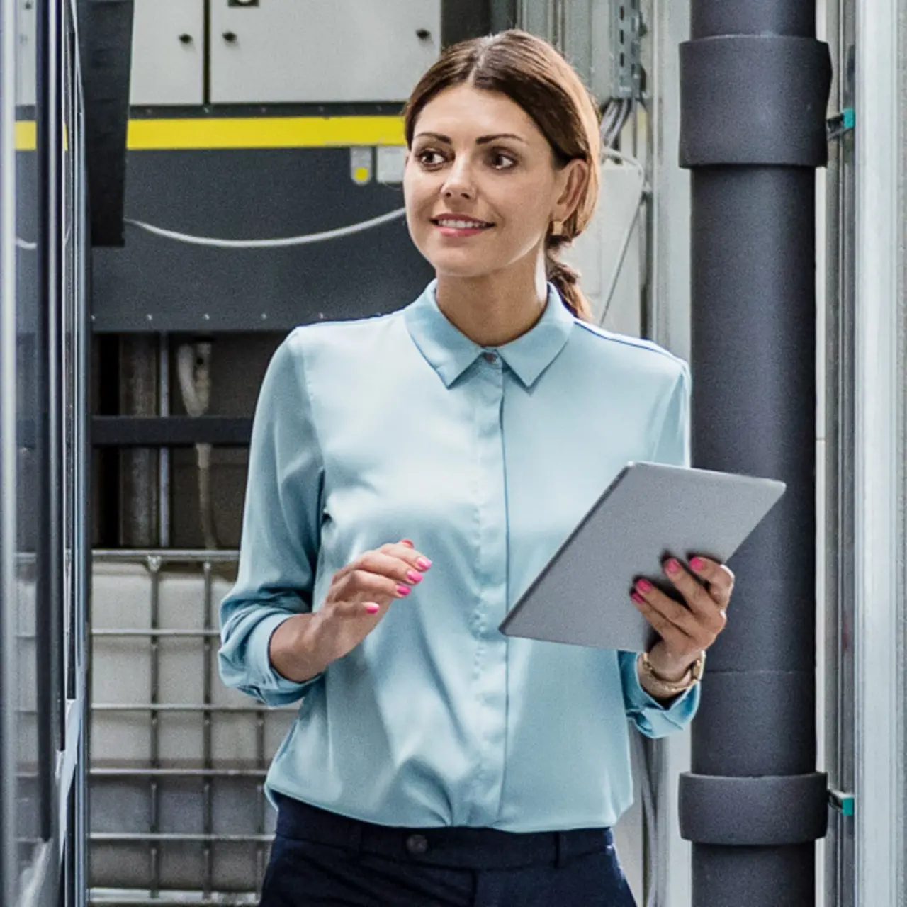 Geschäftsfrau mit Tablet in der Hand prüft Roboterarm in moderner Fabrikhalle