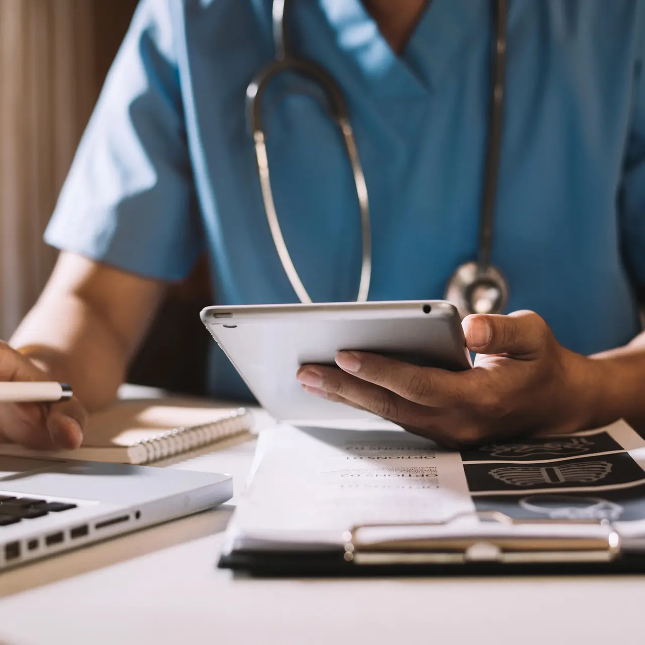 Mediziner sitzt am Schreibtisch und arbeitet auf seinem Tablet