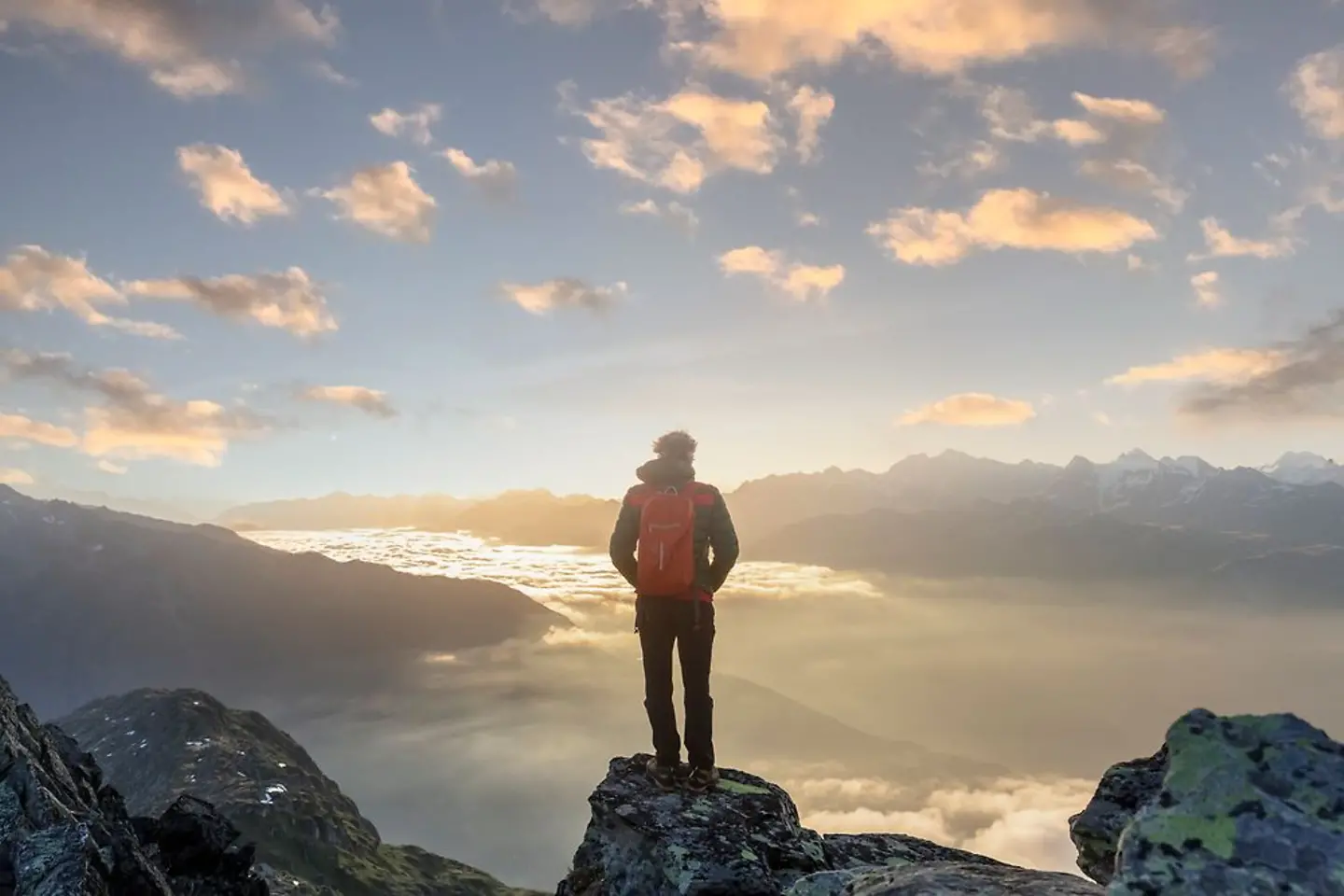 Mann mit Rucksack steht auf einem Berg vor der aufgehenden Sonne